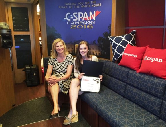Daisy Colvin displays her certificate of Merit while sitting with Comcast VP Kristen Roberts inside the C-SPAN bus.