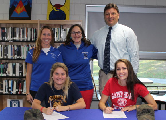 Sydney Cowell (seated left) and Anna Mesham (seated right) sign National Letters of Intent proudly watched by (from left to right) Lyme-Old Lyme High School (LOLHS) Athletic Director Hildie Heck, LOLHS Girls' Lacrosse Coach Emily Maciano and LOLHS Principal Jim Wygonik. standing, 